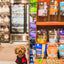 Instinct Raw Boost Mixers freeze dried dog food displayed on store shelves with a small brown dog wearing a red and black jacket nearby